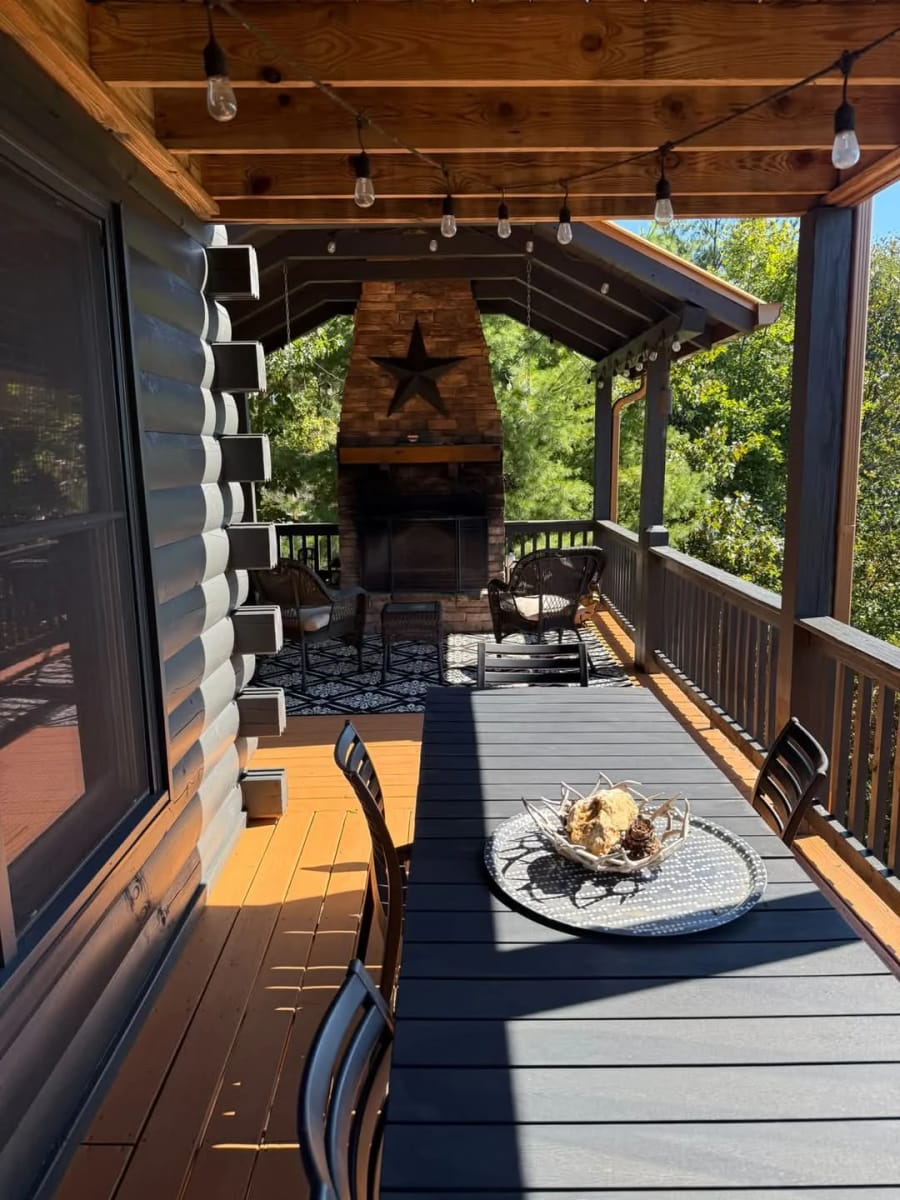 Clean covered porch and deck with a stone fireplace on a log cabin